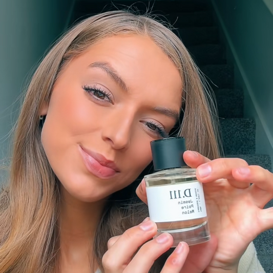 A person holding a bottle of D.111 perfume, showcasing its sleek design and label, with a staircase in the background.