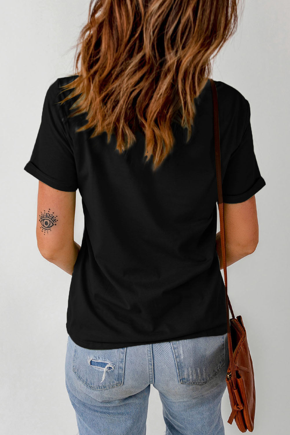 Black graphic cuffed sleeve round neck tee worn by a person with long hair, seen from the back, paired with light blue jeans.