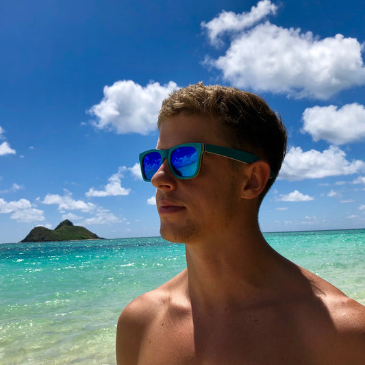 Lanikai Nalu sunglasses on a man at the beach, with turquoise water and a tropical island in the background.